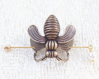 May include: A gold-toned bee brooch with a pearl accent. The bee is detailed with textured wings and a segmented body.