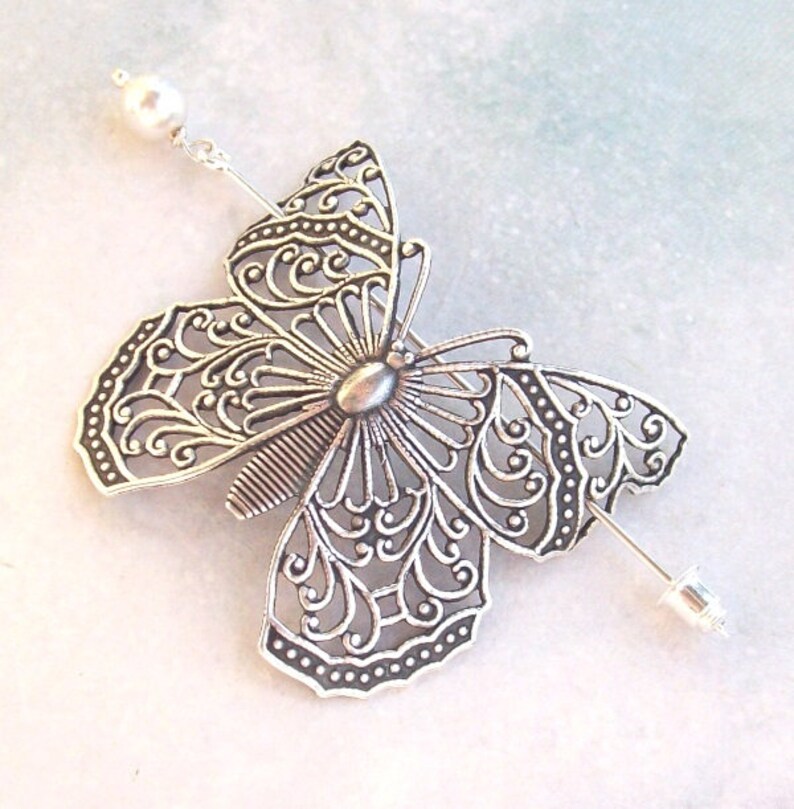 May include: Silver filigree butterfly hair pin with a pearl accent. The butterfly is detailed with intricate swirls and patterns.