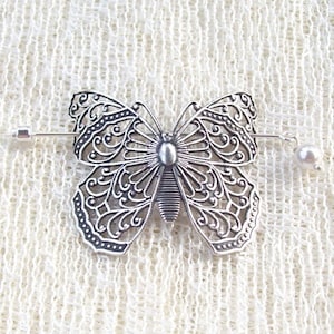 May include: Silver filigree butterfly hair clip with a pearl accent. The clip is attached to a silver bar with a pin on one end and a pearl on the other.