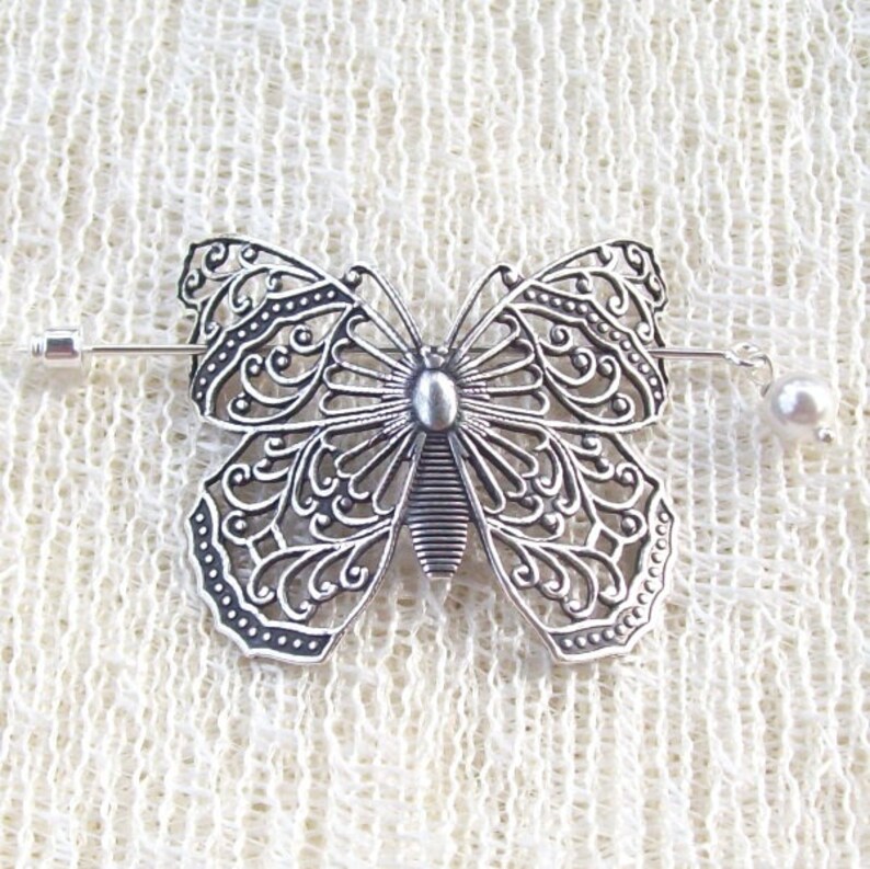 May include: Silver filigree butterfly hair clip with a pearl accent. The clip is attached to a silver bar with a pin on one end and a pearl on the other.