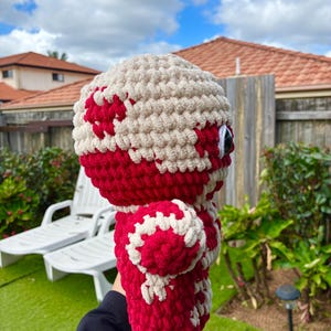 Puede incluir: Una mu&ntilde;eca de peluche hecha a mano, con cabeza y cuerpo redondos. La mu&ntilde;eca es principalmente roja con detalles blancos, incluido un patr&oacute;n en la cabeza y el cuerpo. Tiene ojos grandes, negros y blancos. La mu&ntilde;eca est&aacute; hecha de un hilo suave y texturizado.