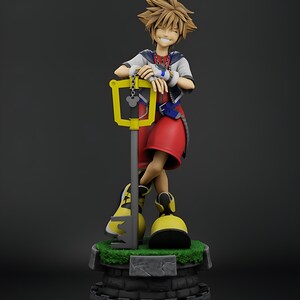 May include: A figurine of a smiling character with spiky brown hair, red shorts, and yellow shoes, leaning on a large yellow key. The figure stands on a stone base with green grass.