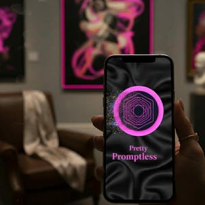 May include: A smartphone displays a pink and purple geometric design with the text "Pretty Promptless" on a black background. The phone is held in front of artwork in a gallery setting, with a brown leather armchair and abstract paintings in the background.