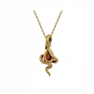 May include: A gold-toned metal necklace featuring a pendant shaped like a coiled snake with textured scales. The snake wraps around a central, teardrop-shaped, deep red gemstone. The pendant hangs from a matching gold-toned link chain.