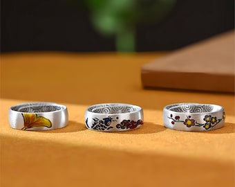 May include: Three silver-toned metal rings featuring detailed enamel designs. The first ring displays a yellow ginkgo leaf, the second shows a blue koi fish with red clouds, and the third features a branch with small red and yellow flowers.