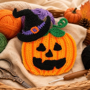 May include: A crocheted orange pumpkin with a black witch hat, featuring black yarn eyes, nose, and a jagged mouth. The pumpkin has green crocheted leaves and a vine on top, surrounded by yarn balls, scissors, and a crochet hook in a basket.
