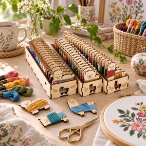 Op de afbeelding: Drie houten opbergdozen met borduurgaren gewikkeld rond diervormige klosjes, waaronder schapen, beren en lama's. De set bevat losse strengen gekleurd garen, een gouden schaar en een borduurring met bloemmotieven.