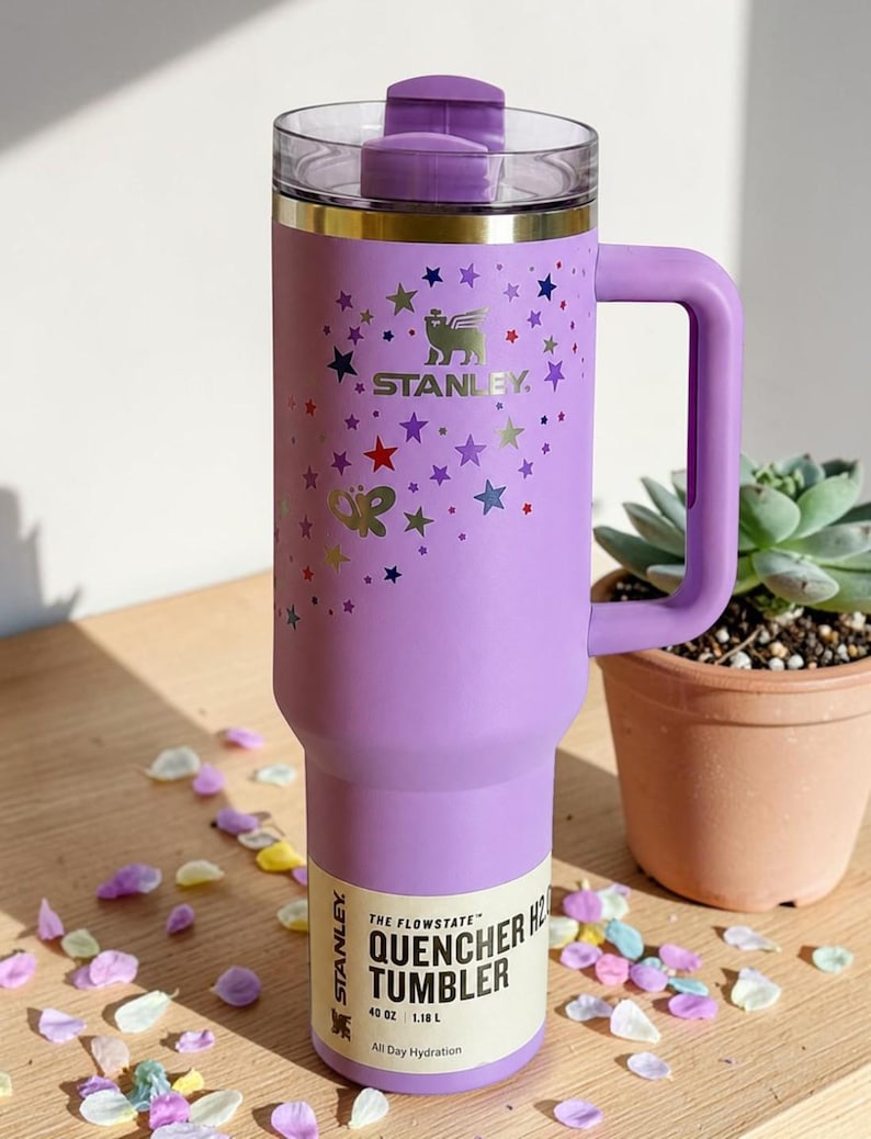 May include: A purple Stanley Flowstate Quencher tumbler with a handle, decorated with colorful stars and a butterfly. The tumbler has a clear lid and a label that reads "Quencher H2.0 Tumbler". It holds 40 oz (1.18 L).