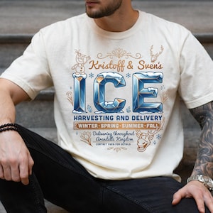 Puede incluir: Una camiseta de manga corta color crema con un estampado gr&aacute;fico que dice Kristoff & Sven's ICE HARVESTING AND DELIVERY. El dise&ntilde;o incluye ilustraciones de un mu&ntilde;eco de nieve, un reno y copos de nieve con letras azules y doradas.