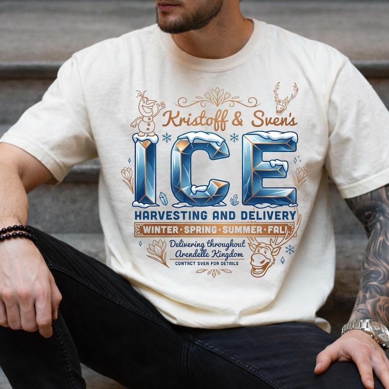 Puede incluir: Una camiseta de manga corta color crema con un estampado gr&aacute;fico que dice Kristoff & Sven's ICE HARVESTING AND DELIVERY. El dise&ntilde;o incluye ilustraciones de un mu&ntilde;eco de nieve, un reno y copos de nieve con letras azules y doradas.