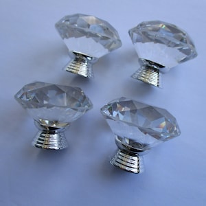 May include: Four clear glass diamond-shaped cabinet knobs with silver metal bases.
