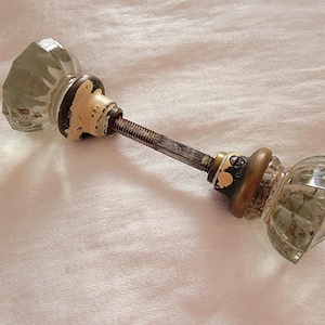 May include: A pair of antique glass door knobs with a metal connecting rod. The knobs are clear glass with a faceted design.