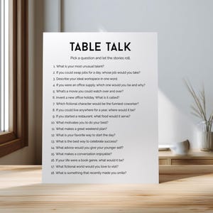 May include: A white card with the title "TABLE TALK" and a list of conversation-starter questions. The card is placed on a wooden table, with a window and a vase of decorative plants in the background.