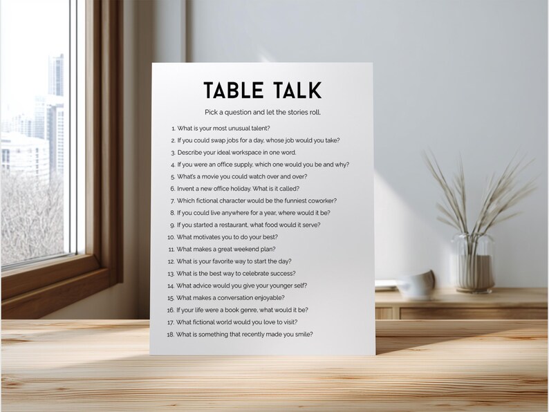 May include: A white card with the title "TABLE TALK" and a list of conversation-starter questions. The card is placed on a wooden table, with a window and a vase of decorative plants in the background.