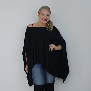 May include: A woman wearing a black off-the-shoulder poncho top with a long-sleeved design, blue jeans, and black over-the-knee boots.