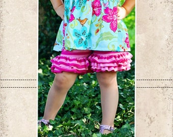 May include: A young girl wearing a blue and pink floral print dress with pink and white striped ruffle shorts. The girl is standing in a grassy area. The image includes the text "CKC Patterns Couture Made Simple" and "CKC Kids".