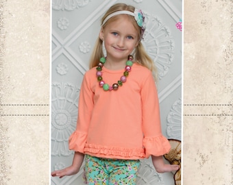 May include: A young girl wearing a peach-colored long-sleeved shirt with ruffled sleeves and hem, paired with floral print pants. She is also wearing a beaded necklace and a headband. The image includes the text "CKC Patterns" and "CKC Kids".