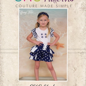 Może przedstawiać: Mała dziewczynka w biało-niebieskim stroju marynarskim z falbaniastą spódnicą i opaską na głowie. Strój zdobią nadruki kotwic i guziki. Dziewczynka stoi na tle plaży z gwiazdą morską.