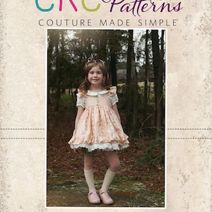 Può includere: Una bambina indossa un vestito rosa floreale con colletto bianco e bordi in pizzo, in un ambiente boschivo. L'immagine include il testo "CKC Patterns" e "CKC Kids". L'abito ha un'estetica vintage.
