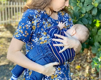 Könnte beinhalten: Eine Frau trägt ein blaues Oberteil mit Blumenmuster und hält ein Baby, das blaue Jeans und ein gestreiftes Shirt trägt. Das Baby trägt blaue und weiße Socken mit der Aufschrift "Good Night Sweet".