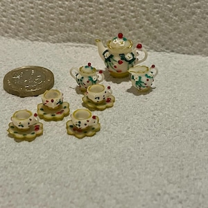 Peut inclure: Un service à thé miniature comprenant une théière, un sucrier, un pot à lait et quatre tasses avec soucoupes assorties. Chaque pièce est blanche avec un motif floral de feuilles vertes et de baies rouges, rehaussé d'un liseré doré, près d'une pièce.