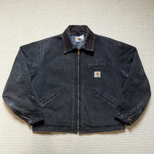 Può includere: Giacca Carhartt nera con colletto in velluto a coste marrone. La giacca ha una chiusura con cerniera, due tasche anteriori e una piccola toppa quadrata con logo sul petto. Realizzata in tessuto resistente in stile workwear.