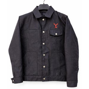 Puede incluir: Chaqueta azul marino oscuro con botones, dos bolsillos en el pecho y dos bolsillos inferiores. La chaqueta tiene un logotipo "Y" rojo en el pecho izquierdo. Colgada de una percha negra.