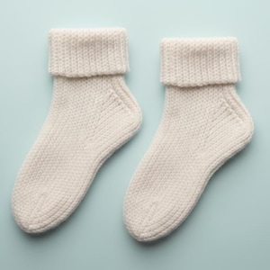 May include: A pair of off-white knitted socks with folded-over cuffs. The socks are made of a textured yarn and are displayed on a light blue background. The socks are a cozy and comfortable accessory.