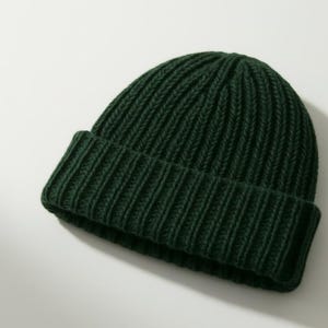 Könnte beinhalten: Eine dunkelgrüne, gerippte Strickmütze. Die Mütze ist am Rand gefaltet und besteht aus einem weichen, strukturierten Material. Die Mütze ist einfarbig und für kaltes Wetter geeignet.