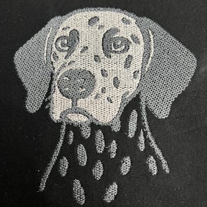 May include: Embroidered image of a Dalmatian dog's head on a black background. The dog's face is white with grey spots, and its ears are grey. The embroidery has a textured appearance, creating a detailed and realistic depiction of the dog.