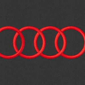 May include: Embroidered red interlocking rings, the Audi logo, on a dark grey background. The design features four connected rings, a symbol of the automotive brand. The stitching is detailed and the colour is vibrant.