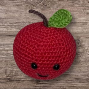 May include: A red crocheted apple with a green crocheted leaf and a smiling face.