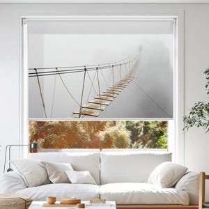 May include: A roller shade featuring a scenic image of a suspension bridge shrouded in fog. The bridge, constructed of wooden planks and supported by cables, stretches into the distance. The image evokes a sense of adventure and mystery, suitable for home decor.