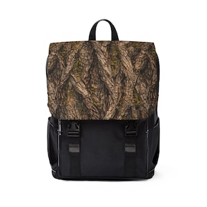 May include: A black backpack with a flap featuring a detailed tree bark pattern in shades of brown, tan, and green. The backpack has a top handle, adjustable straps, and two black buckles on the front.