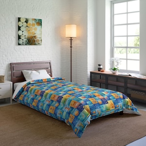 May include: A twin-sized comforter with a colorful, patchwork design featuring marine life and abstract shapes in shades of blue, yellow, and orange. The comforter is on a wooden bed frame in a well-lit room.