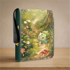 Op de afbeelding: Een rechthoekige verzamelkaartenmap met een groene Bulbasaur-figuur in een weelderige bosrijke omgeving met bloemen en een paddenstoel. De rug is donkergroen met een geel en blauw logo en een zwarte stoffen polsband aan de zijkant.