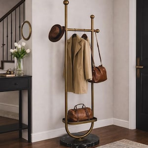Puede incluir: Un perchero de metal dorado con base de mármol negro. Un abrigo beige, un sombrero marrón y un bolso de cuero cuelgan. Una bolsa de viaje de cuero marrón está en el estante inferior. En una entrada.