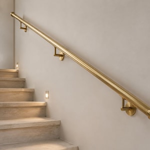 May include: A cylindrical brass handrail mounted to a wall with three matching circular brackets. The handrail features a smooth, polished finish and ends with a decorative cap that has three horizontal grooves, providing a secure grip.