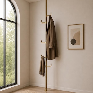 May include: A floor-to-ceiling tension-mounted coat rack in a brushed brass finish. The vertical pole features multiple protruding hooks at varying heights, currently holding a brown wool coat and a matching brown fringed scarf.