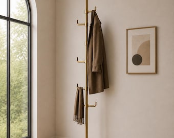 May include: A floor-to-ceiling tension-mounted coat rack in a brushed brass finish. The vertical pole features multiple protruding hooks at varying heights, currently holding a brown wool coat and a matching brown fringed scarf.