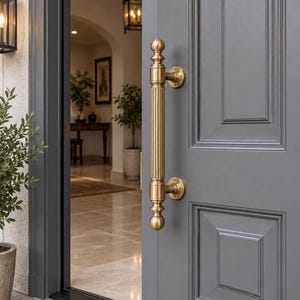May include: A vertical brass door handle with a fluted cylindrical grip and spherical finials at both ends, mounted onto a dark gray paneled door with two circular base plates secured by visible screws, featuring a metallic gold finish.