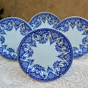May include: A set of four round ceramic plates featuring a white center and a wide, intricate blue border with floral and scrollwork patterns. The plates are arranged in a cluster, showcasing the consistent blue and white decorative design.