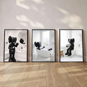 Könnte beinhalten: Ein Set aus drei gerahmten Wandbildern, die eine schwarze Zeichentrickfigur in einem weißen Badezimmer zeigen. Das erste Bild zeigt die Figur beim Zähneputzen, das zweite in einer Badewanne und das dritte beim Lesen eines Buches.