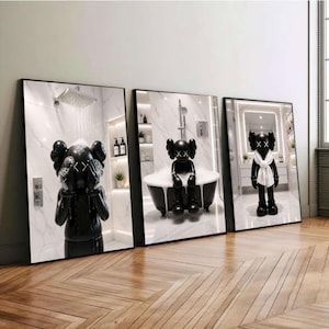 Könnte beinhalten: Drei gerahmte Wandbilder mit einer schwarzen KAWS-Figur in einem Badezimmer. Das erste zeigt die Figur unter einer Dusche, das zweite sitzend in einer Badewanne und das dritte stehend in einem Badezimmer mit einem weißen Handtuch um den Hals.