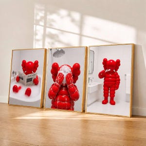Könnte beinhalten: Ein Set aus drei gerahmten Drucken, die eine leuchtend rote Zeichentrickfigur in einem Badezimmer zeigen. Das erste Bild zeigt die Figur in einer Badewanne beim Zeitunglesen, das zweite beim Gesichtwaschen und das dritte beim Zähneputzen.