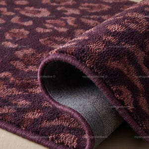 Op de afbeelding: Een rechthoekig tapijt met een luipaardprint in donkerpaars en mauve. Het tapijt heeft een dikke, getufte poolstructuur en een afgewerkte rand. Eén hoek van het tapijt is omgeslagen, waardoor een donkergrijze, gestructureerde achterkant zichtbaar is.