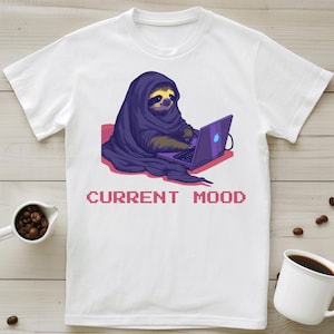 May include: A white short-sleeved t-shirt featuring a graphic of a sloth wrapped in a dark purple blanket while using a purple laptop. Below the illustration, the text CURRENT MOOD is printed in a pink pixelated font style on the front of the shirt.