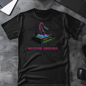 May include: Black t-shirt featuring a pixelated graphic of a dragon atop a router, with the text "ACCESS DENIED" in pink. The dragon is pink and black, with blue and green flames. The router is black with green and blue lights.