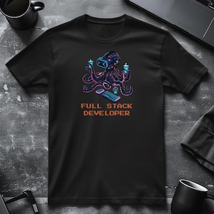 Op de afbeelding: Zwart t-shirt met een kleurrijke octopus die een VR-headset draagt, drankjes vasthoudt en een toetsenbord en muis gebruikt. De tekst "FULL STACK DEVELOPER" staat eronder in oranje pixellettertype.