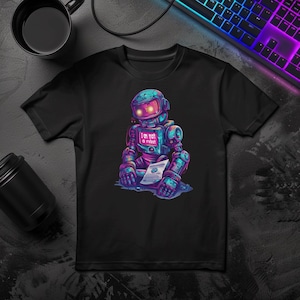 May include: A black short-sleeved t-shirt featuring a graphic of a blue and purple robot with glowing yellow eyes. The robot has a screen on its chest displaying the text 'I am not a robot' and is holding a white paper document with a blue icon.